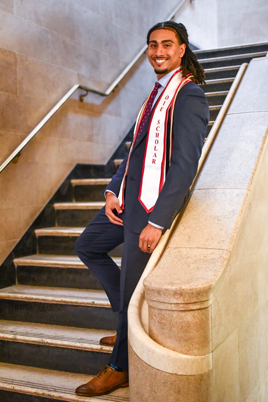 Jakobi in a suit and OIE Scholar stole on a staircase at his Cornell graduation