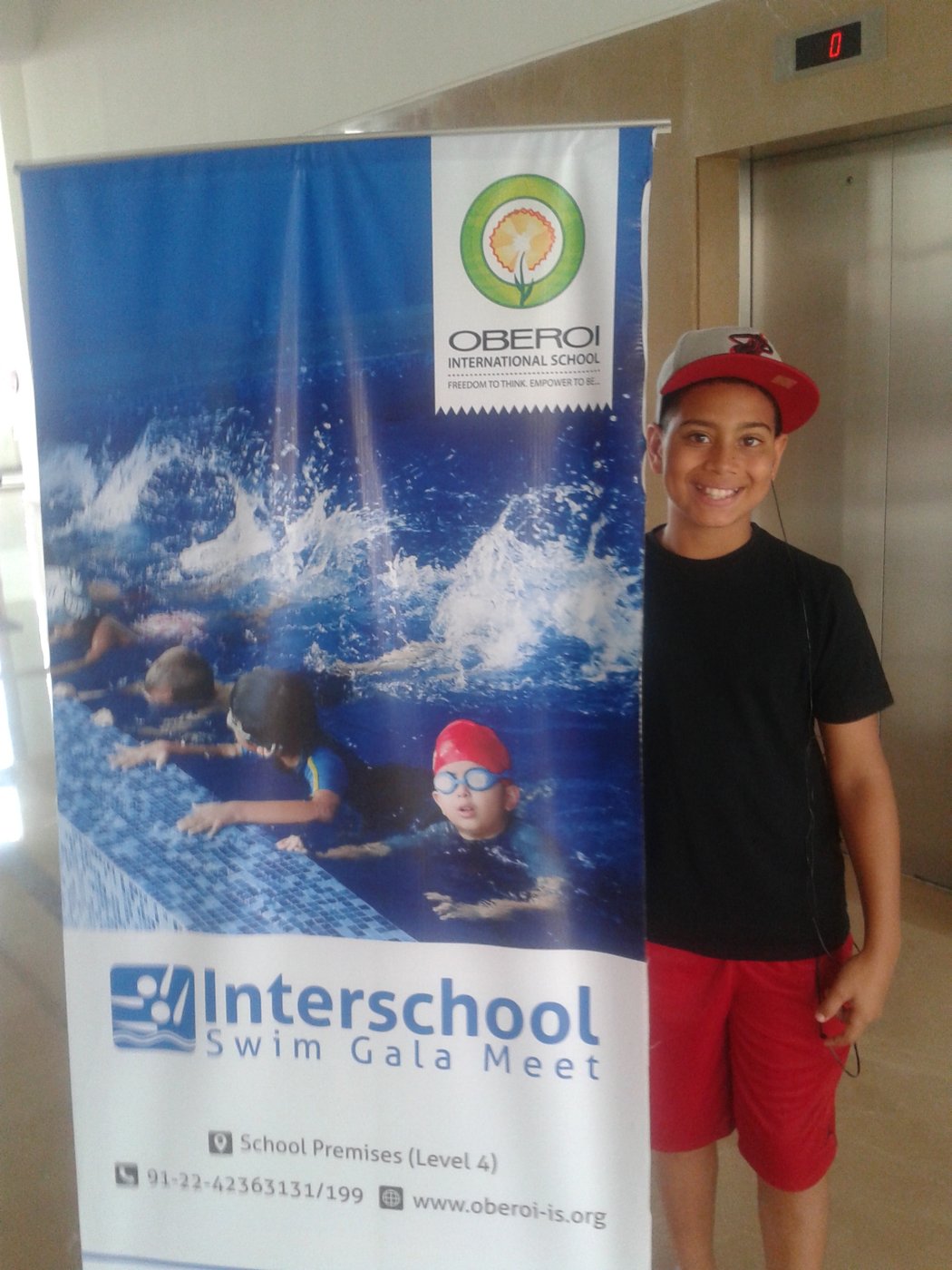 Jakobi in fifth grade beside an Oberoi International School swim meet banner in Mumbai